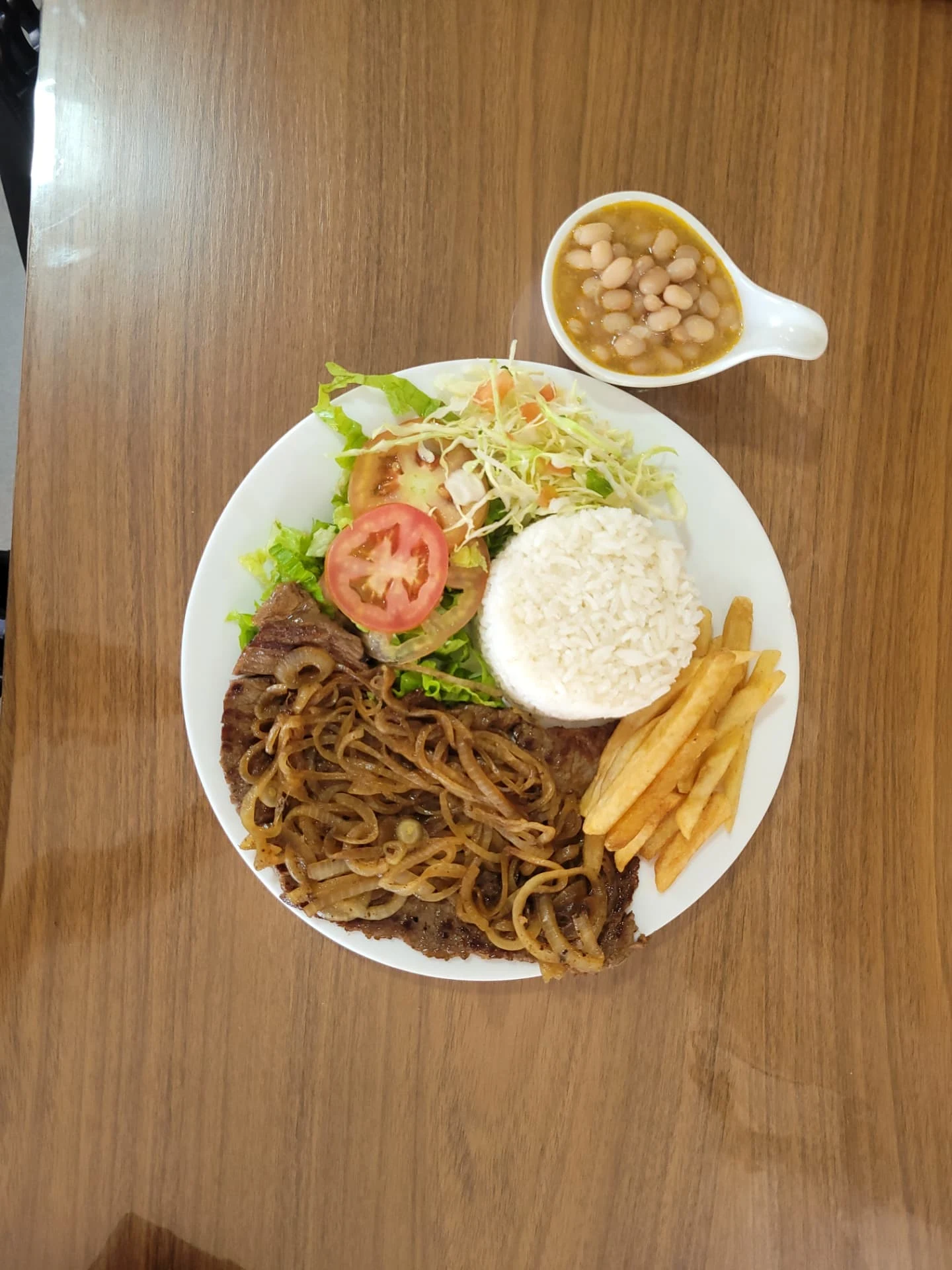 Prato com carne coberta de cebolas, arroz, batata frita e salada no Flavia's Restaurante
